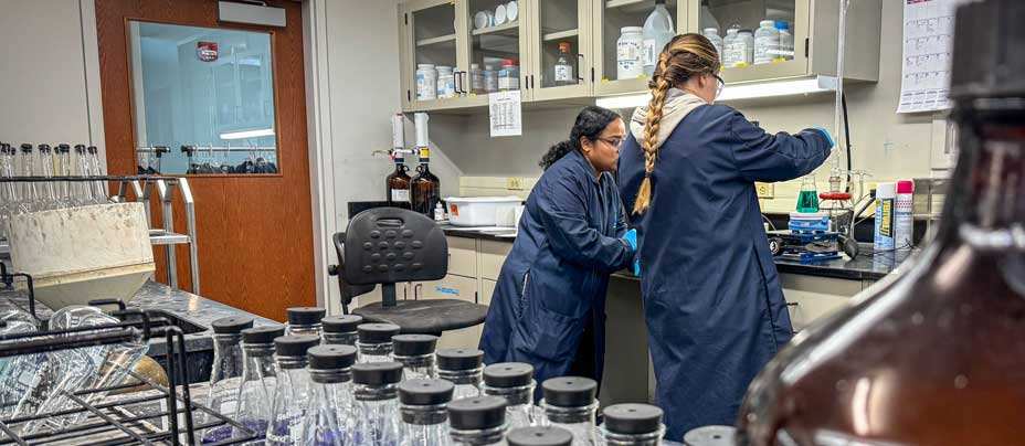 Two women in blue safety coats using lab equipment to test water samples